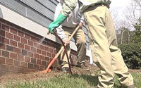 Two men in khaki pants are aerating a lawn.